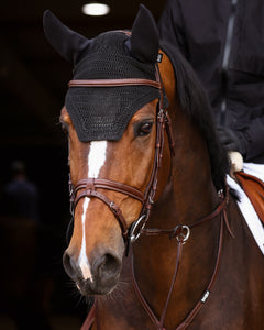 Man in equestrian attire standing next to a brown horse indoors.